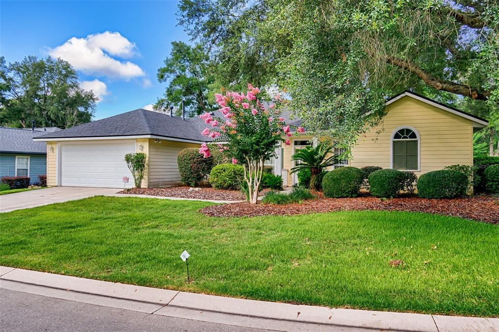 A single-story yellow house with a two-car garage, a front lawn, and a blooming tree — 6618 SW 83RD TERRACE, GAINESVILLE, FL