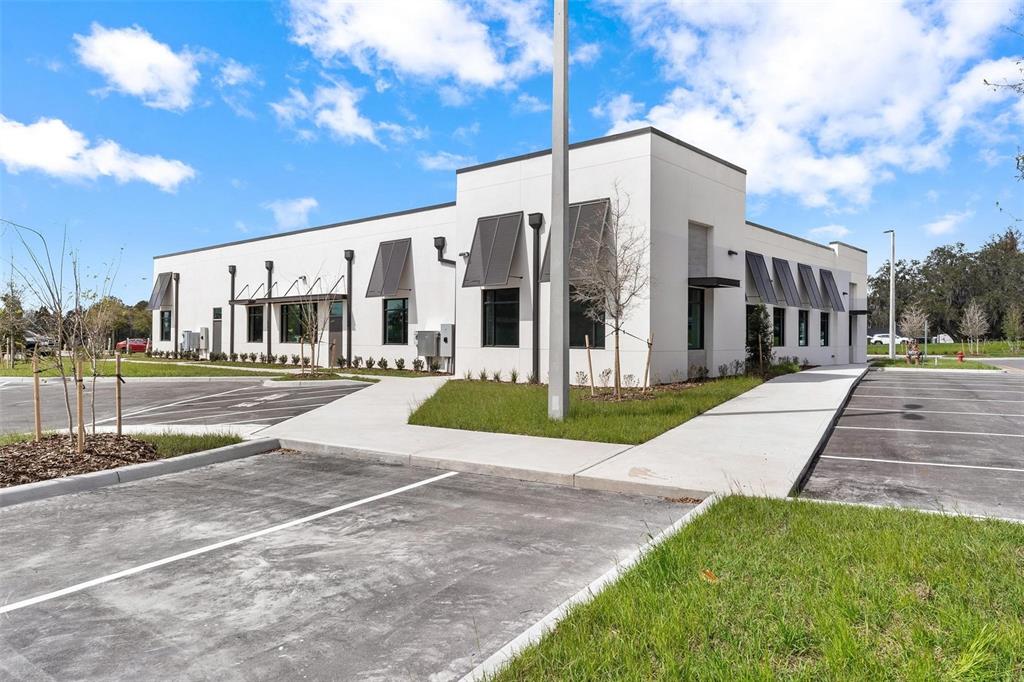 A modern, single-story commercial building with white exterior walls and dark metal window awnings — 10941 NE 89TH DRIVE, THE VILLAGES, FL