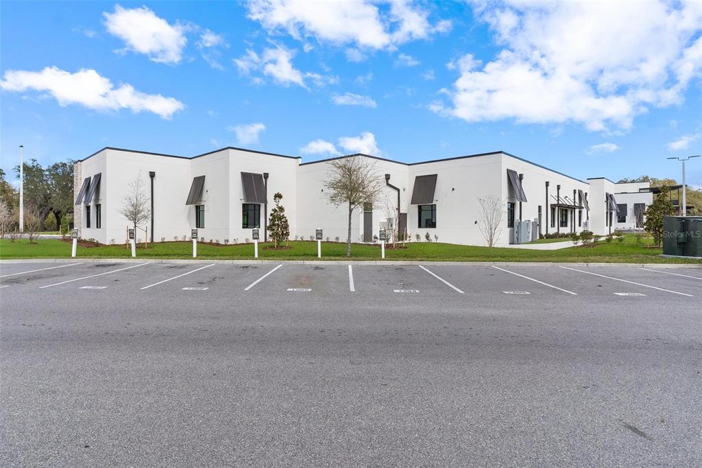 A modern, white single-story commercial building sits behind a paved parking lot under a blue sky — 10941 NE 89TH DRIVE, THE VILLAGES, FL