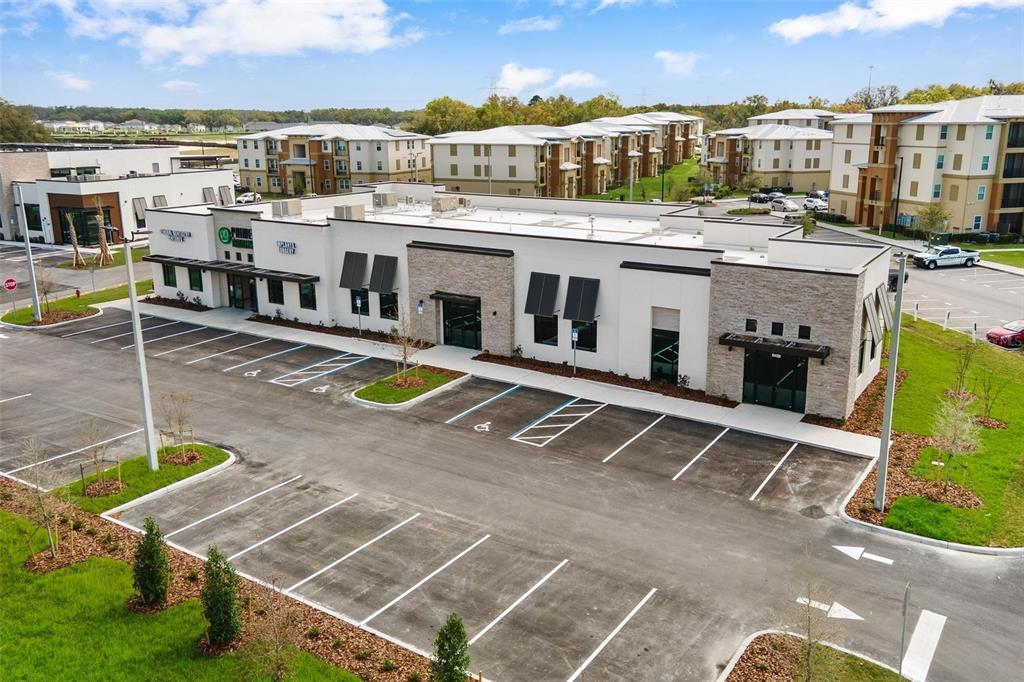 An aerial view shows a modern commercial building with a parking lot and surrounding apartments — 10941 NE 89TH DRIVE, THE VILLAGES, FL