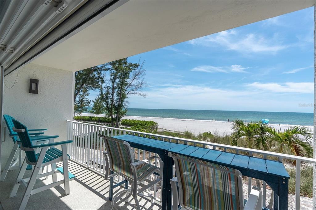 A balcony with outdoor seating overlooks a sandy beach and the ocean under a blue sky — 20204 GULF BOULEVARD UNIT 3, INDIAN SHORES, FL