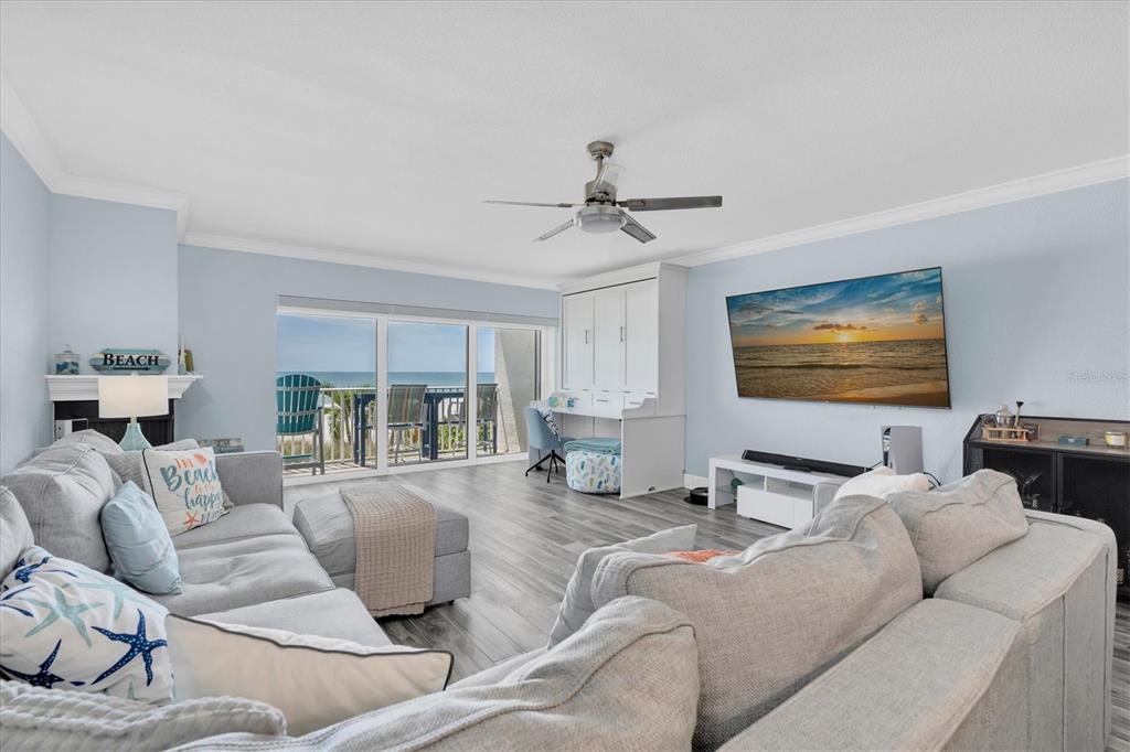 A living room features light blue walls, gray wood-look flooring, a sectional sofa, and balcony views — 20204 GULF BOULEVARD UNIT 3, INDIAN SHORES, FL