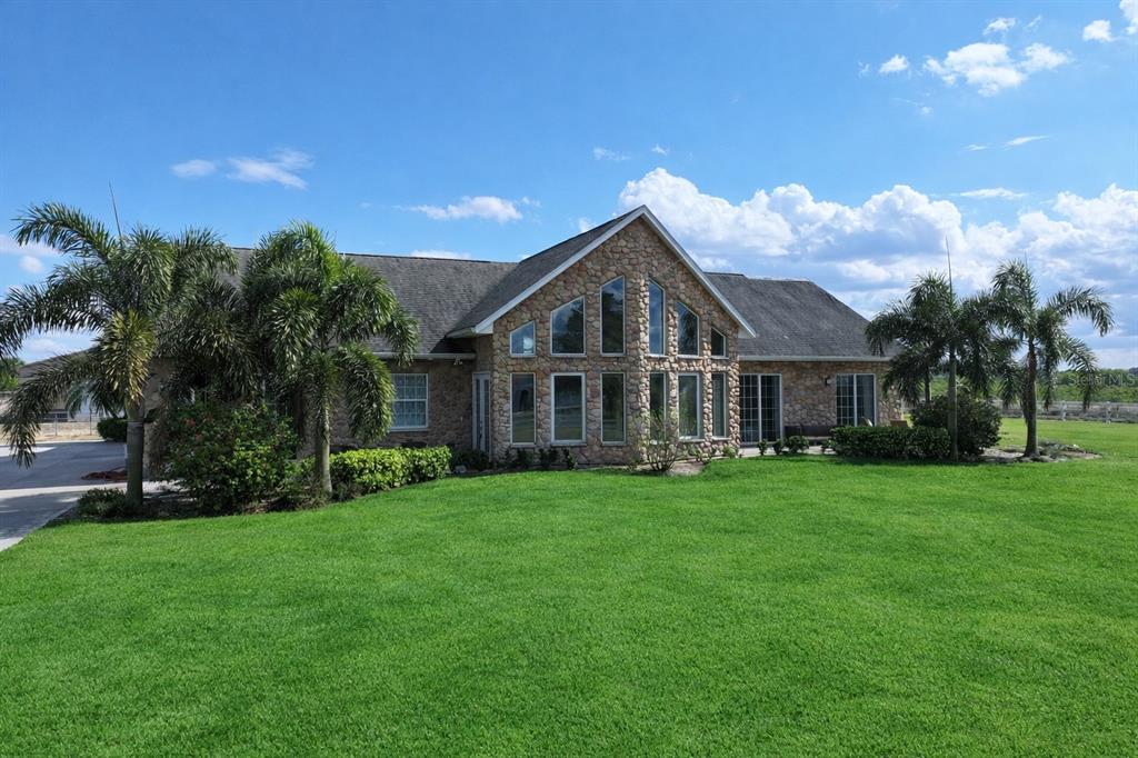 A stone-faced house with a large triangular window feature sits on a grassy lawn — 186 S BEAR POINTE DRIVE, LAKE PLACID, FL