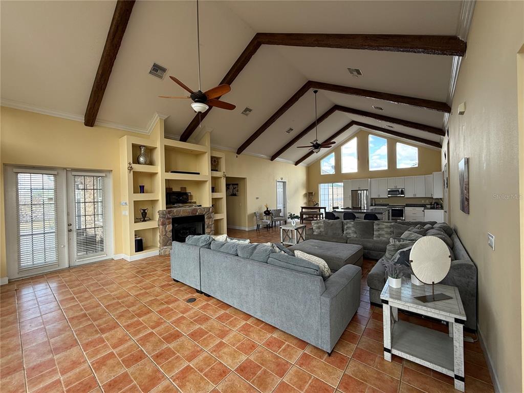 A spacious living room features vaulted ceilings with exposed beams, a stone fireplace, and tile flooring — 186 S BEAR POINTE DRIVE, LAKE PLACID, FL