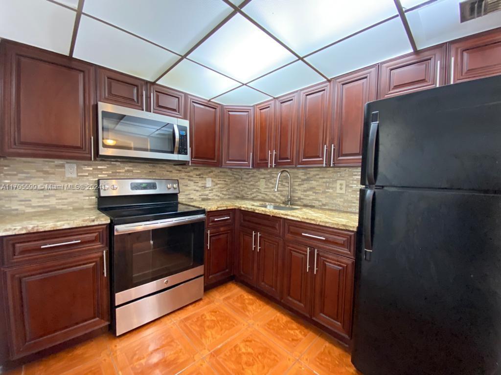A kitchen features dark wood cabinets, stainless steel appliances, a black refrigerator, and tile flooring — 15600 NW 7th Ave # 520, Miami FL 33169, MIAMI, FL