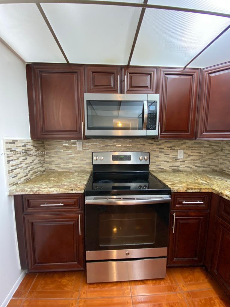 A kitchen features dark wood cabinets, stainless steel appliances, granite countertops, and a tiled backsplash — 15600 NW 7th Ave # 520, Miami FL 33169, MIAMI, FL