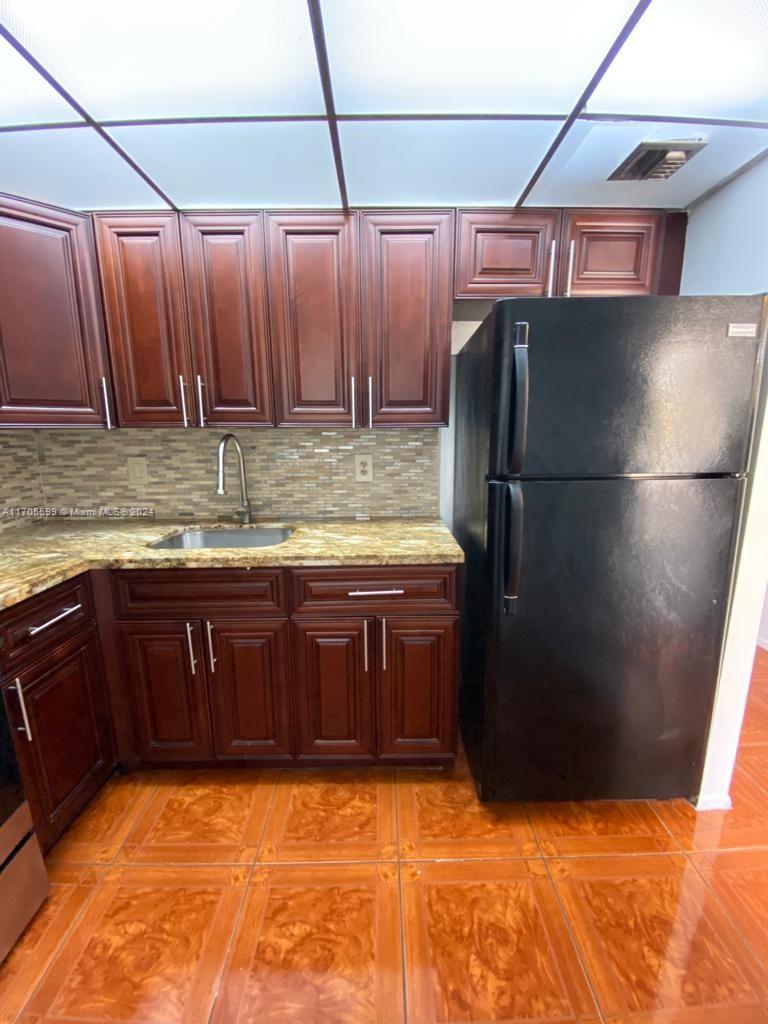 A kitchen features dark wood cabinets, granite countertops, a black refrigerator, and orange tiled flooring — 15600 NW 7th Ave # 520, Miami FL 33169, MIAMI, FL