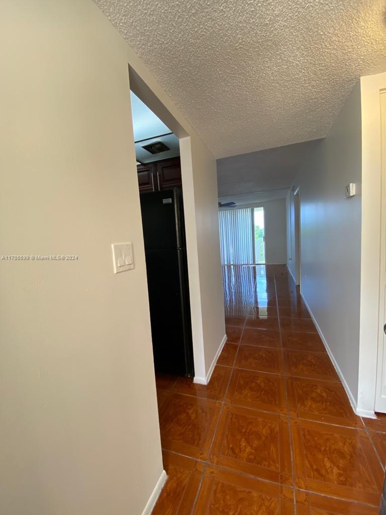 A hallway with brown tile flooring leads toward a kitchen and a bright living area — 15600 NW 7th Ave # 520, Miami FL 33169, MIAMI, FL
