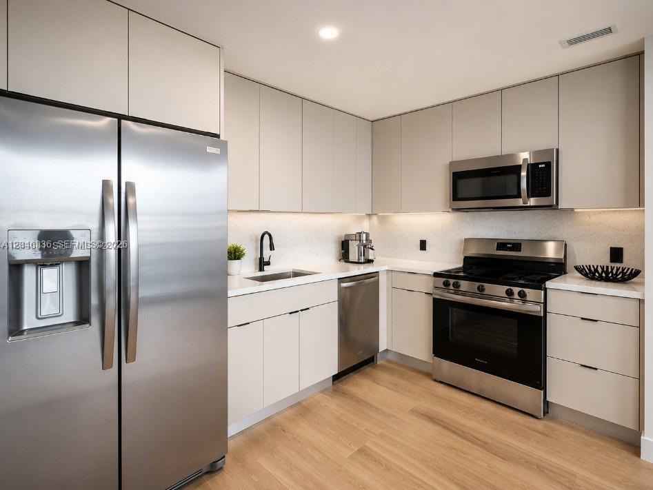 A modern kitchen features stainless steel appliances, light-colored cabinetry, and wood-look flooring — 300 S Biscayne Blvd # 1503, Miami FL 33131, MIAMI, FL