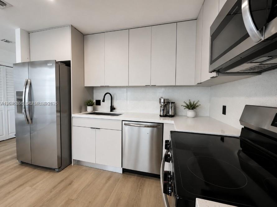 A modern kitchen features white cabinets, stainless steel appliances, and light wood-look flooring — 300 S Biscayne Blvd # 1503, Miami FL 33131, MIAMI, FL