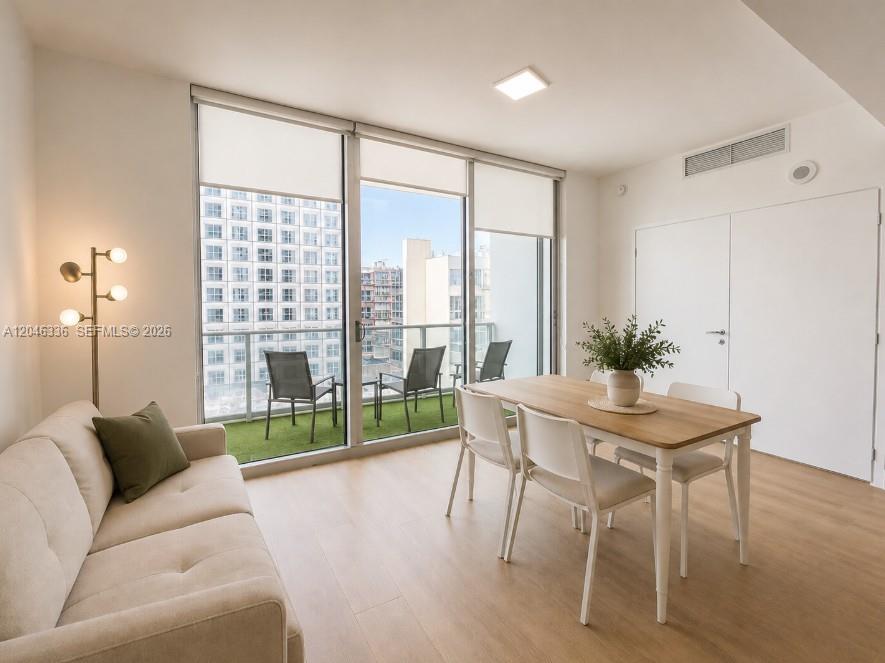 A living and dining area features light wood flooring, a sofa, and a balcony view — 300 S Biscayne Blvd # 1503, Miami FL 33131, MIAMI, FL