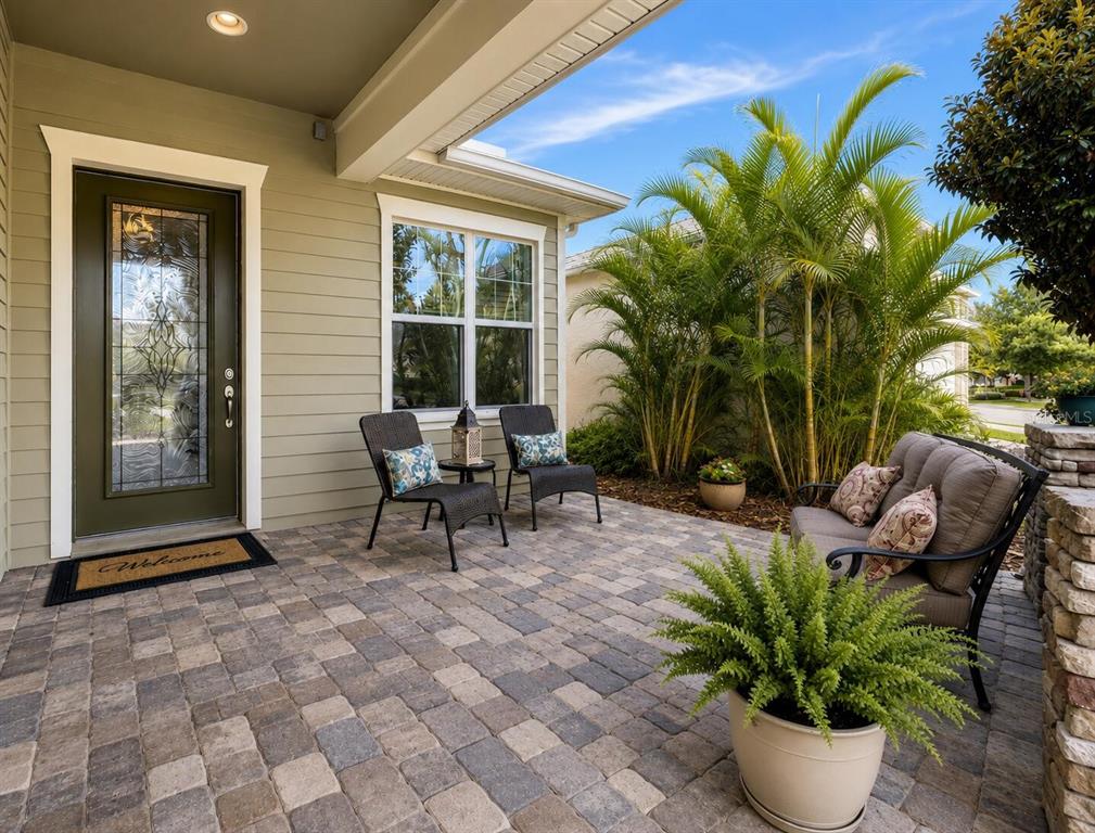 A covered front porch features paver flooring, outdoor seating, and a glass-paneled front door — 13928 SWALLOW HILL DRIVE, LITHIA, FL