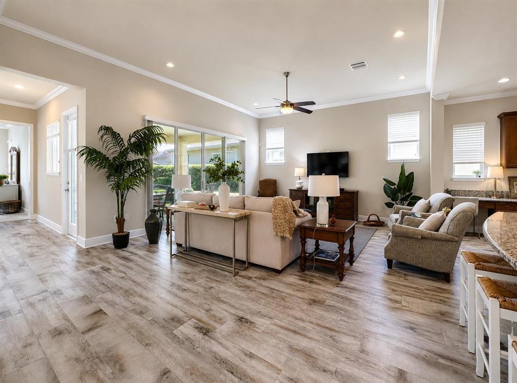 A spacious living room features light wood-look tile flooring, a beige sofa, and sliding doors — 13928 SWALLOW HILL DRIVE, LITHIA, FL