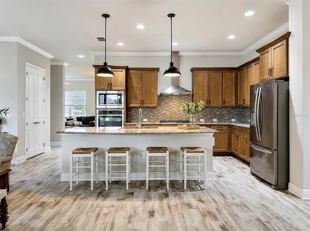 A kitchen with wood cabinets, granite countertops, a center island with stools, and stainless appliances — 13928 SWALLOW HILL DRIVE, LITHIA, FL