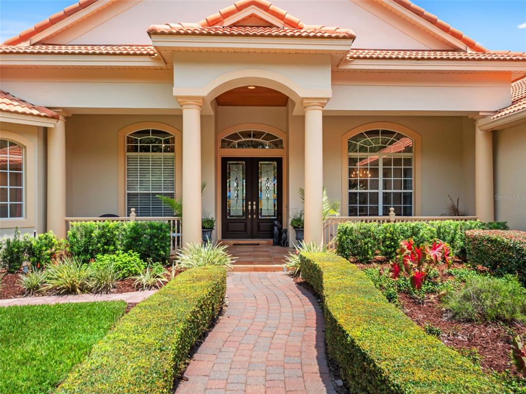 The front exterior of a house features a brick walkway, manicured hedges, and double doors — 32516 HAWKS LAKE LANE, SORRENTO, FL