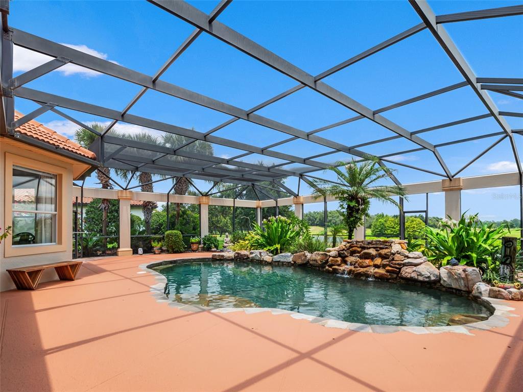 A screened-in patio features a freeform swimming pool with a rock waterfall and landscaping — 32516 HAWKS LAKE LANE, SORRENTO, FL
