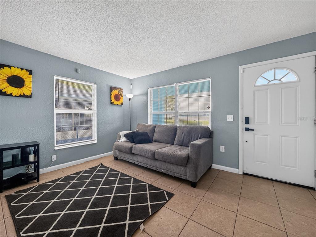 A living room features a gray sofa, a patterned rug, tile flooring, and sunflower wall art — 1155 W 5TH STREET, LAKELAND, FL