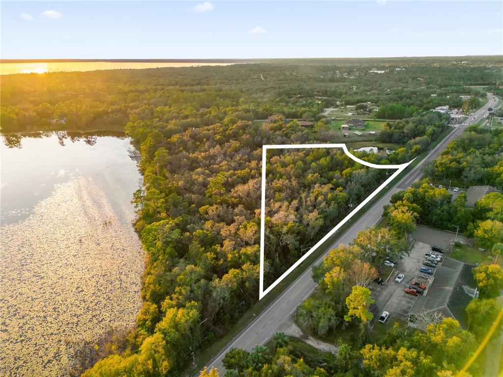 An aerial view shows a wooded lot outlined in white next to a road and lake — 1785 DOYLE ROAD, DELTONA, FL
