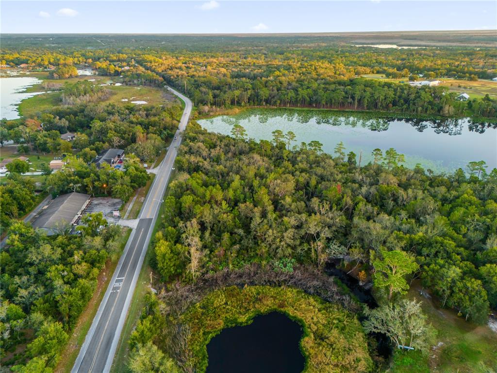 An aerial view shows a road running past a wooded area with two ponds — 1785 DOYLE ROAD, DELTONA, FL