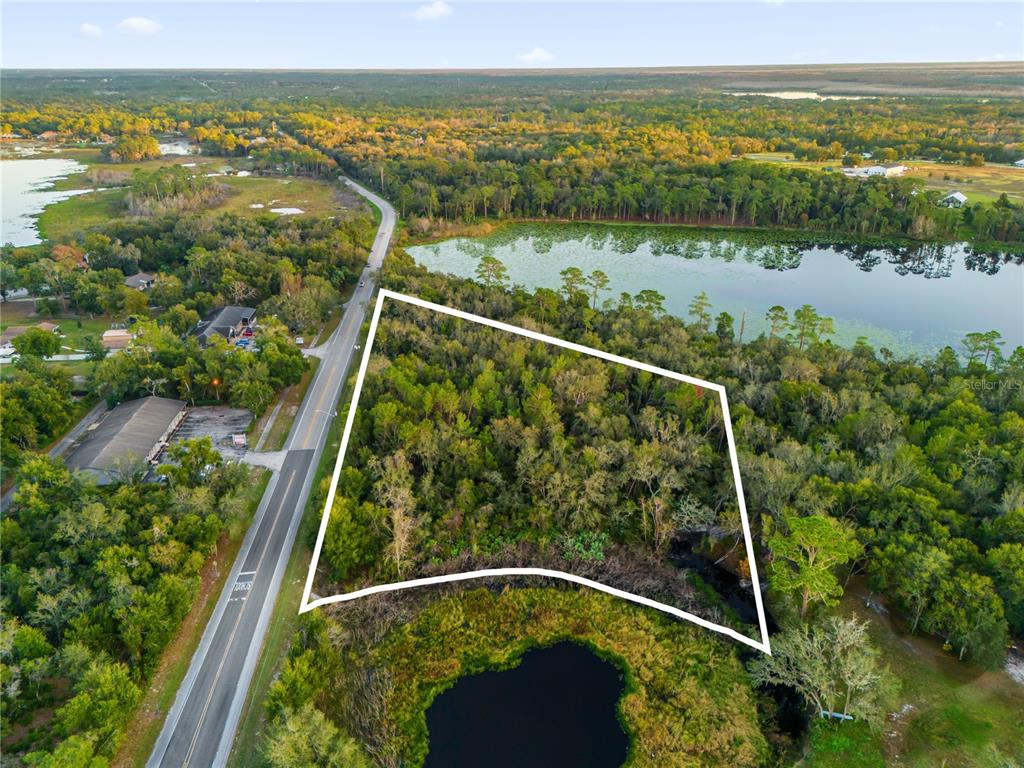 An aerial view shows a wooded, irregularly shaped lot bordered by a road and water — 1785 DOYLE ROAD, DELTONA, FL
