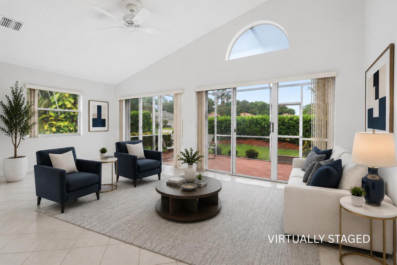 A virtually staged living room features a vaulted ceiling, tile floors, and large sliding glass doors — 10884 Royal Caribbean Circle, Boynton Beach FL 33437, BOYNTON BEACH, FL