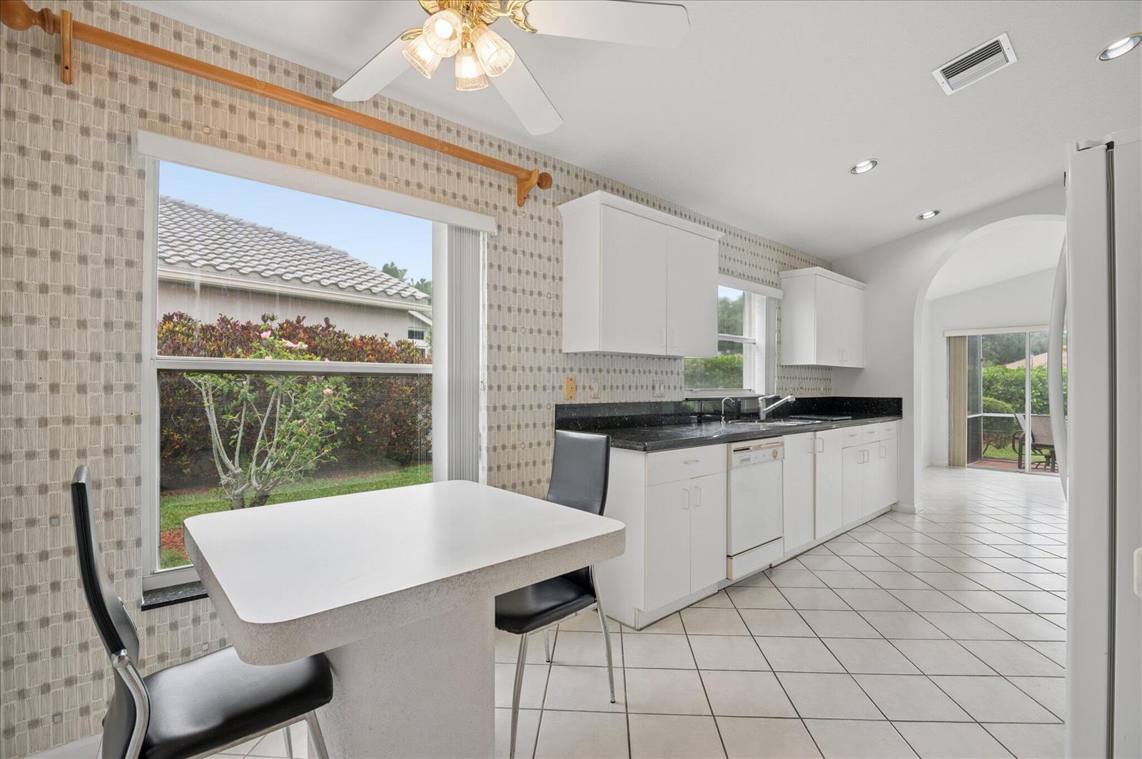 A kitchen with white cabinets, black countertops, tiled floors, and a small dining table — 10884 Royal Caribbean Circle, Boynton Beach FL 33437, BOYNTON BEACH, FL