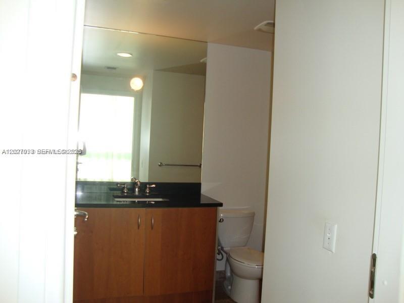 A bathroom features a wooden vanity with a black countertop, a large mirror, and toilet — 300 S Biscayne Blvd # 2909, Miami FL 33131, MIAMI, FL