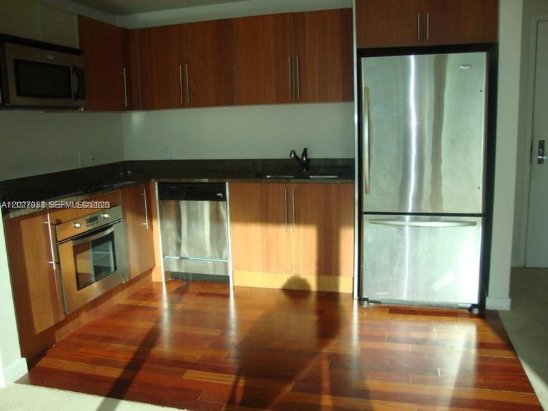 A kitchen features wood cabinets, stainless steel appliances, dark countertops, and hardwood flooring — 300 S Biscayne Blvd # 2909, Miami FL 33131, MIAMI, FL