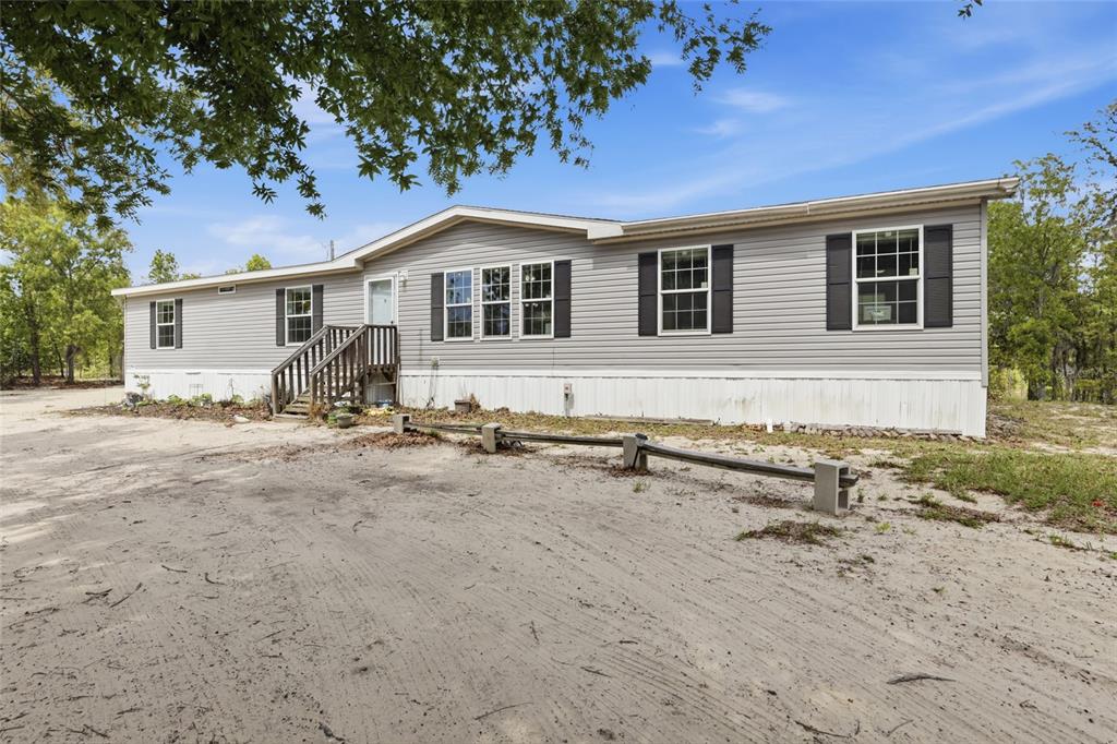 A light gray manufactured home sits on a sandy lot with a wooden front staircase — 2640 NE 74TH AVENUE, HIGH SPRINGS, FL