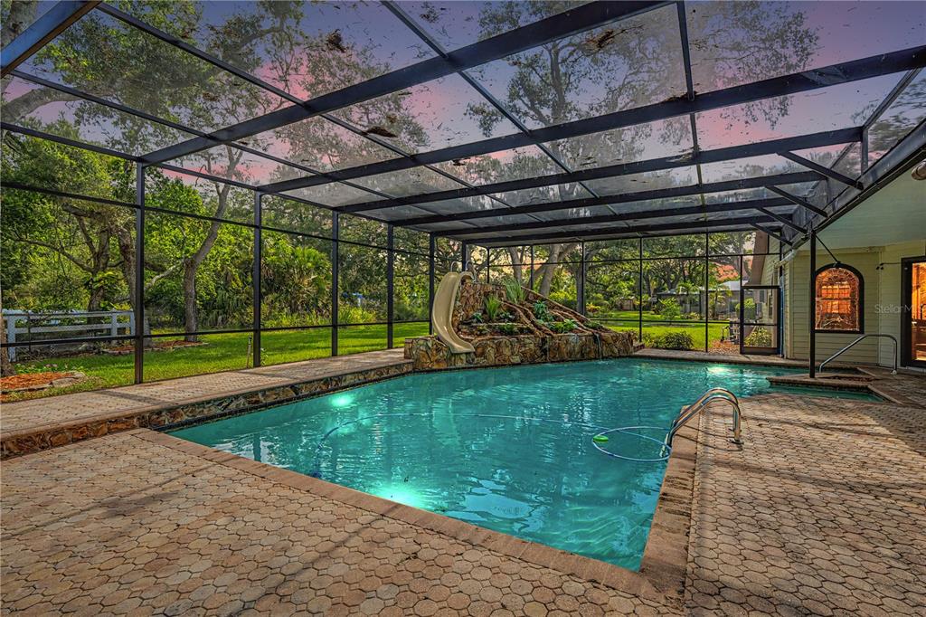 A screened-in swimming pool features a stone waterfall and slide in a backyard setting — 2160 LAURENCE DRIVE, CLEARWATER, FL