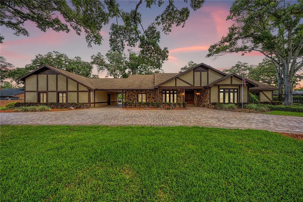 A single-story Tudor-style house with stone accents and a large paver driveway at sunset — 2160 LAURENCE DRIVE, CLEARWATER, FL