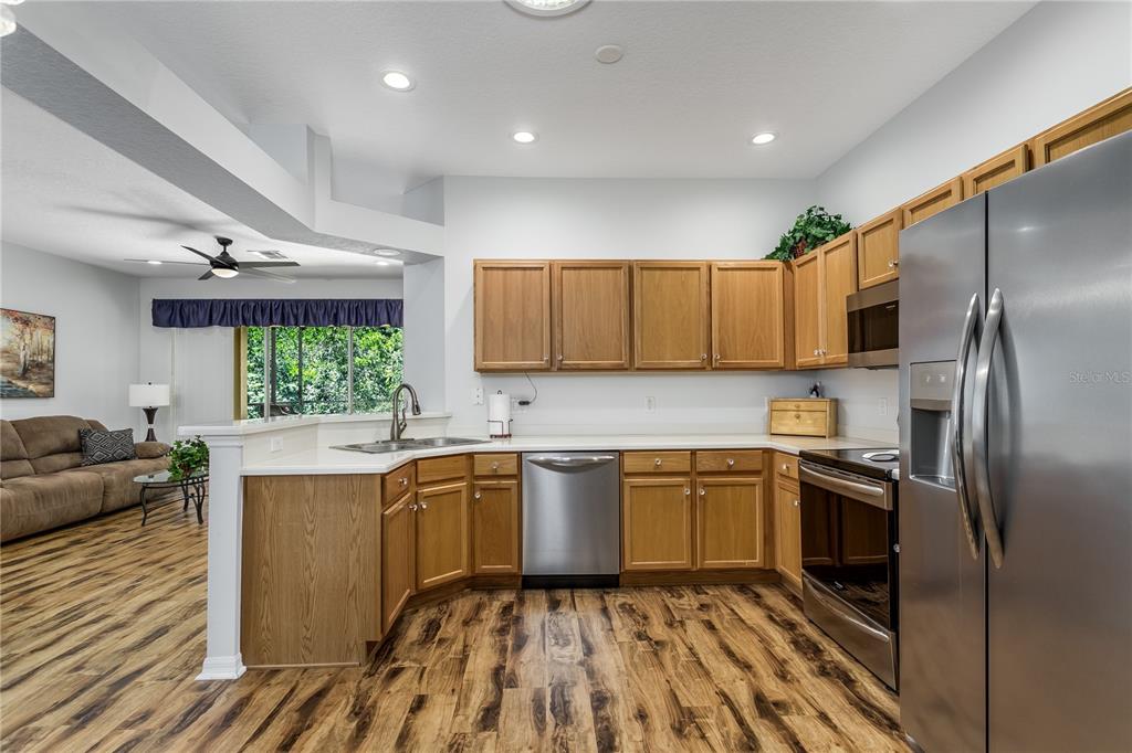 A kitchen with wood cabinets, stainless steel appliances, and wood-look flooring opens to a living area — 7235 CLEOPATRA DRIVE, LAND O LAKES, FL
