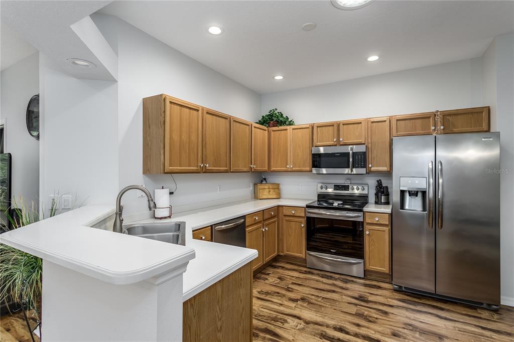 A kitchen features wood cabinets, stainless steel appliances, white countertops, and wood-look flooring — 7235 CLEOPATRA DRIVE, LAND O LAKES, FL