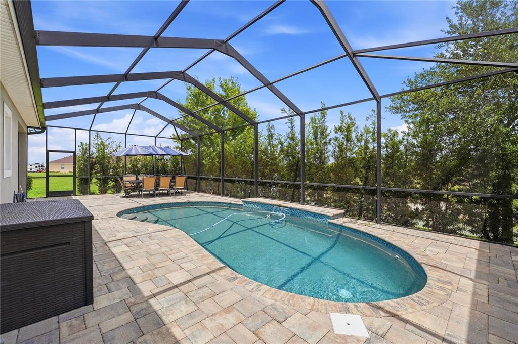 A screened-in patio features a kidney-shaped swimming pool, paver decking, and outdoor dining furniture — 539 WATERFERN TRAIL DRIVE, AUBURNDALE, FL