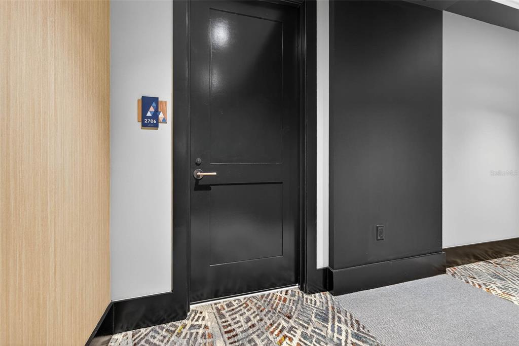 A black door with a room number sign is set between a wood-paneled wall and a dark-painted wall — 275 1ST AVE S UNIT 2706, ST PETERSBURG, FL