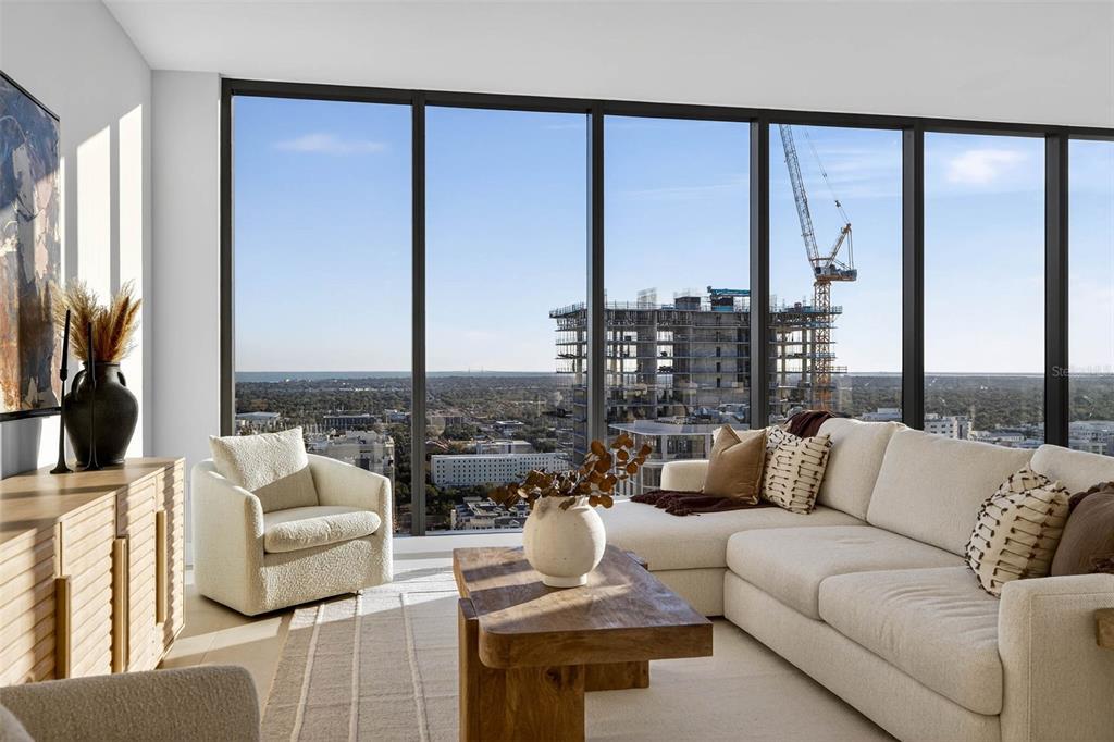 A living room with a cream sectional, accent chair, and floor-to-ceiling windows overlooking a construction site — 275 1ST AVE S UNIT 2706, ST PETERSBURG, FL