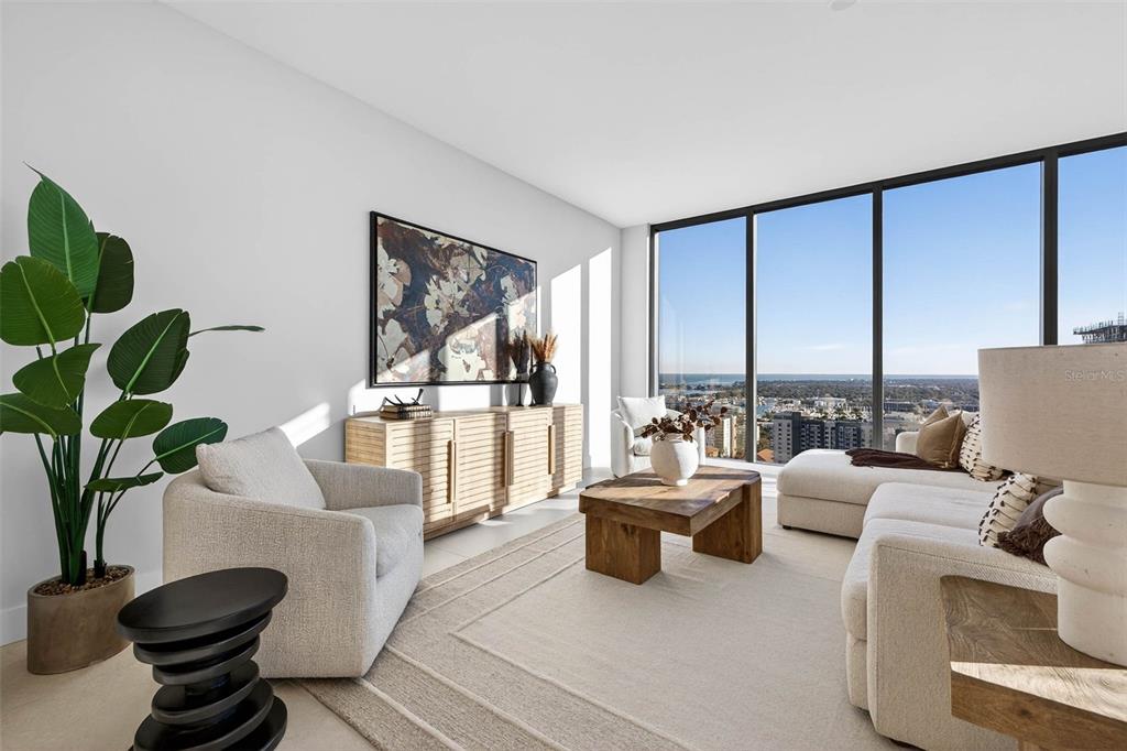 A modern living room features floor-to-ceiling windows with a view and neutral-toned furniture — 275 1ST AVE S UNIT 2706, ST PETERSBURG, FL