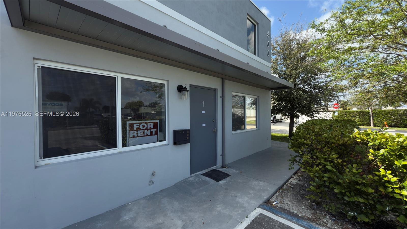 The exterior of a gray commercial building features a front door labeled with the number one — 500 NE 25th St # 1, Pompano Beach FL 33064, POMPANO BEACH, FL