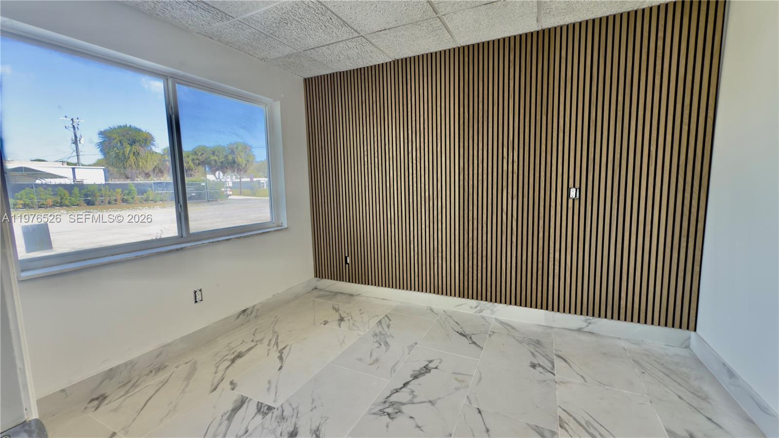 An empty room features white marble-look tile flooring, a wood-slat accent wall, and a window — 500 NE 25th St # 1, Pompano Beach FL 33064, POMPANO BEACH, FL