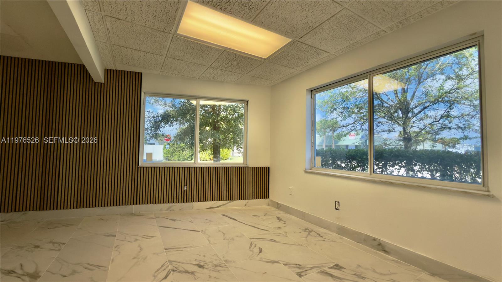 An empty office room features white marble-look tile floors, wood slat wall paneling, and windows — 500 NE 25th St # 1, Pompano Beach FL 33064, POMPANO BEACH, FL