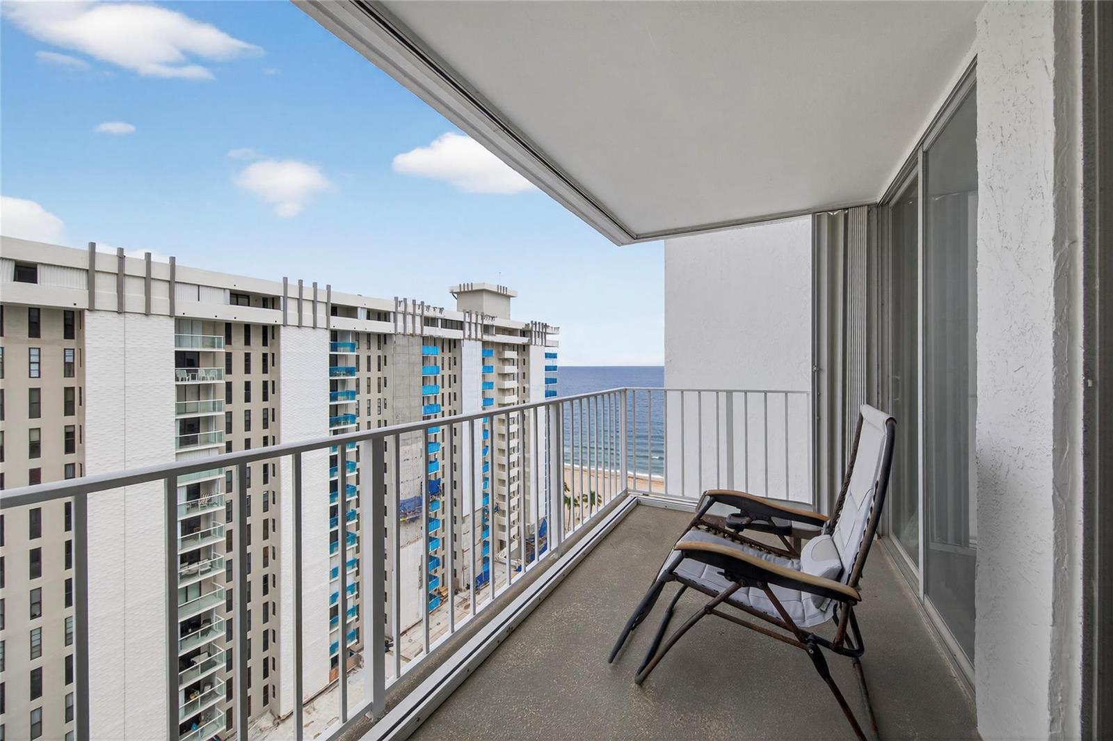 A balcony with a folding chair overlooks a neighboring high-rise building and the ocean — 1010 S Ocean Boulevard # 1711, Pompano Beach FL 33062, POMPANO BEACH, FL