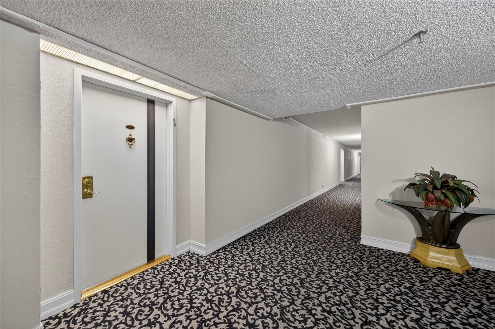 A hallway with patterned carpet, a white door, and a glass-topped console table — 1010 S Ocean Boulevard # 1711, Pompano Beach FL 33062, POMPANO BEACH, FL