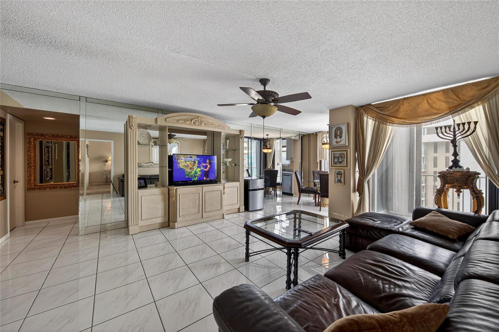 A living room with white tile floors, a leather sectional, and a mirrored wall — 1010 S Ocean Boulevard # 1711, Pompano Beach FL 33062, POMPANO BEACH, FL