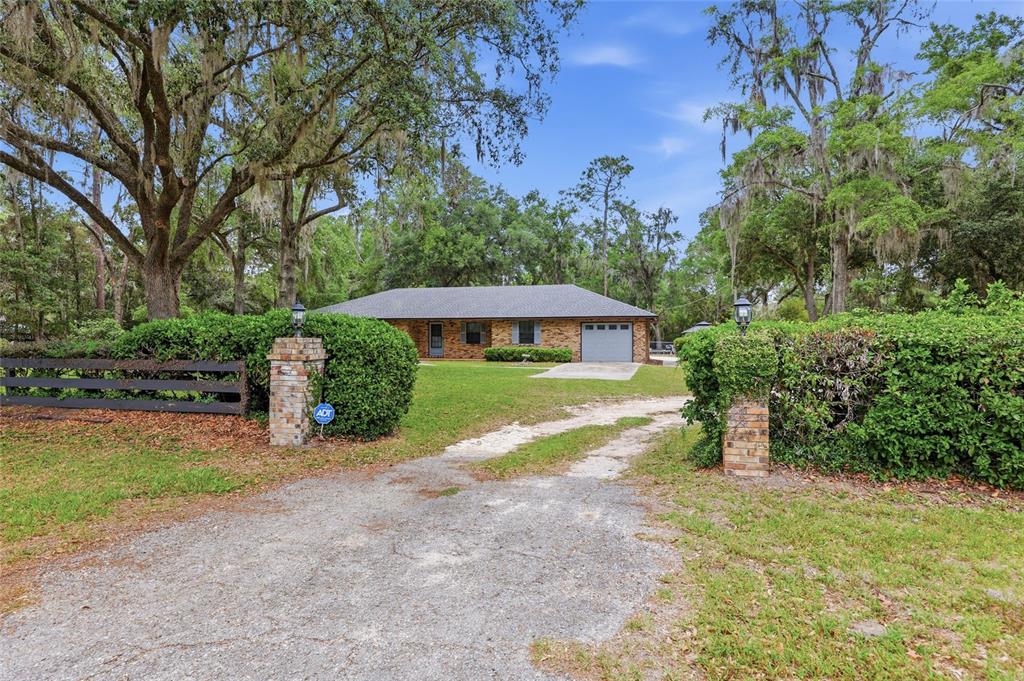A brick ranch-style house sits behind a gravel driveway and a gated entrance with hedges — 4803 W STATE ROAD 238, LAKE BUTLER, FL