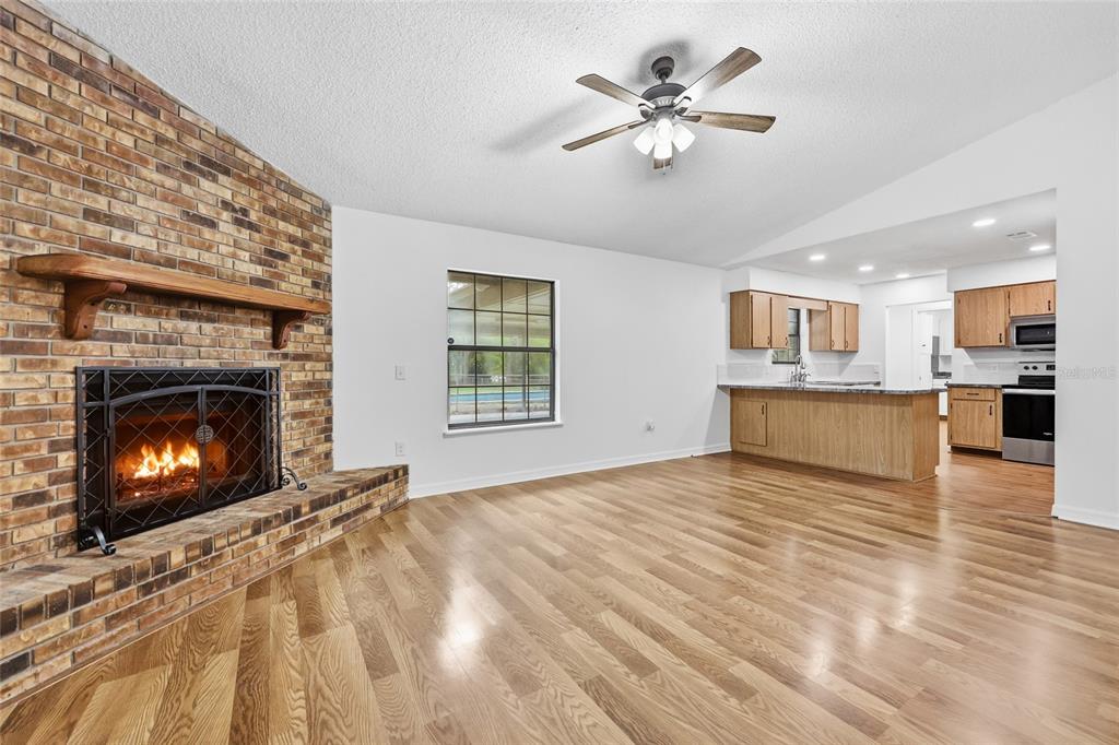 A living room with a brick fireplace, hardwood floors, and an open kitchen with cabinets — 4803 W STATE ROAD 238, LAKE BUTLER, FL