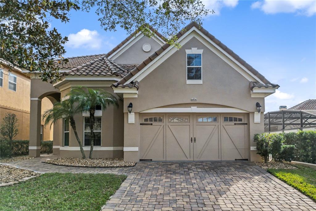 A beige stucco house with a tiled roof, a two-car garage, and a paver driveway — 6976 LUCCA STREET, ORLANDO, FL