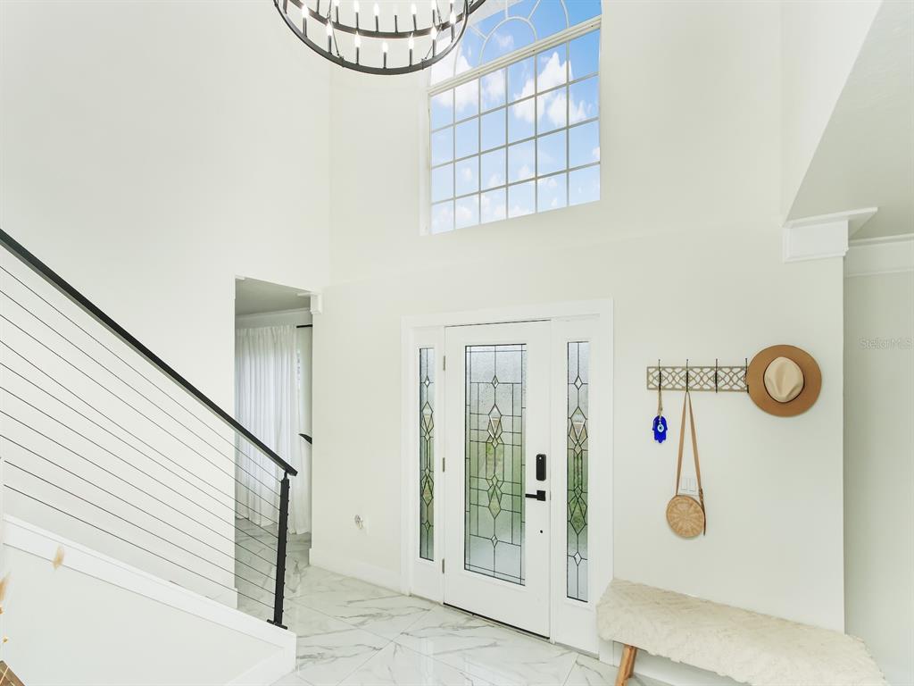 A bright entryway features a high ceiling, a staircase with cable railings, and marble flooring — 7561 LAKE ANDREA CIRCLE, MOUNT DORA, FL
