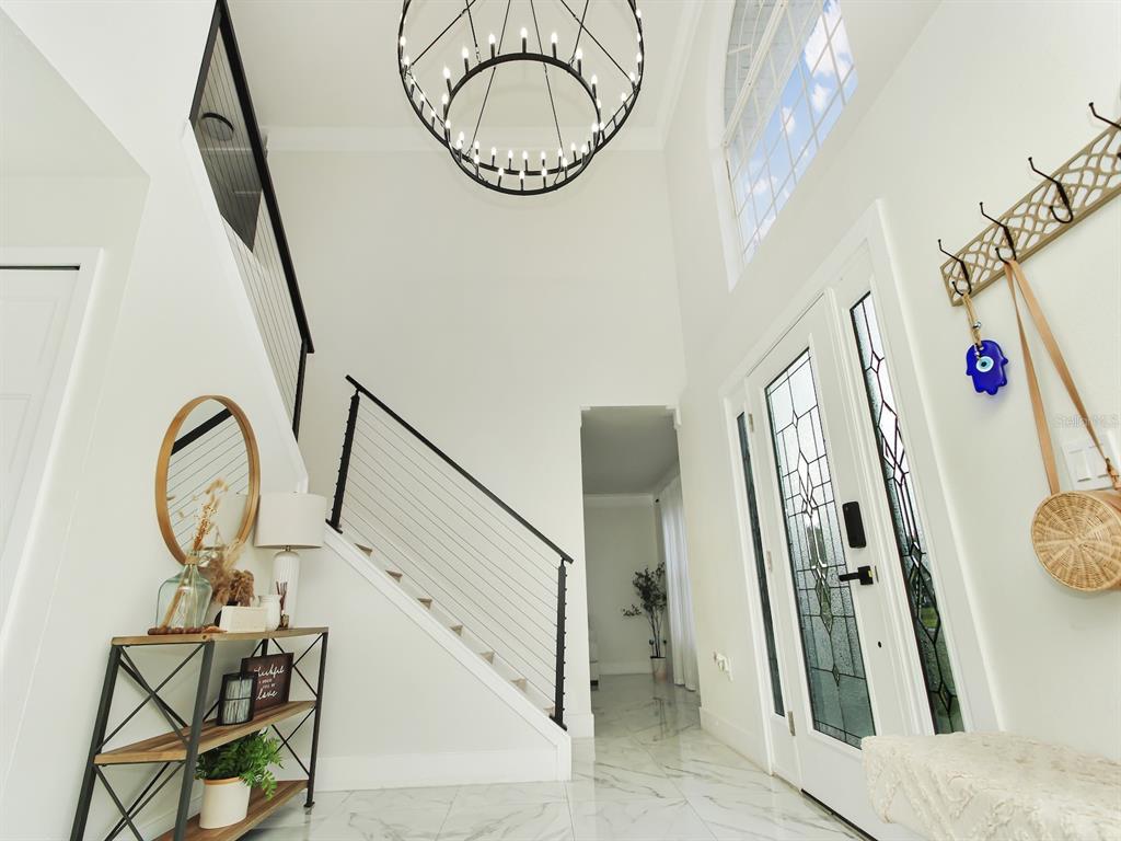 A bright entryway features a modern chandelier, marble-style flooring, and a staircase with cable railings — 7561 LAKE ANDREA CIRCLE, MOUNT DORA, FL