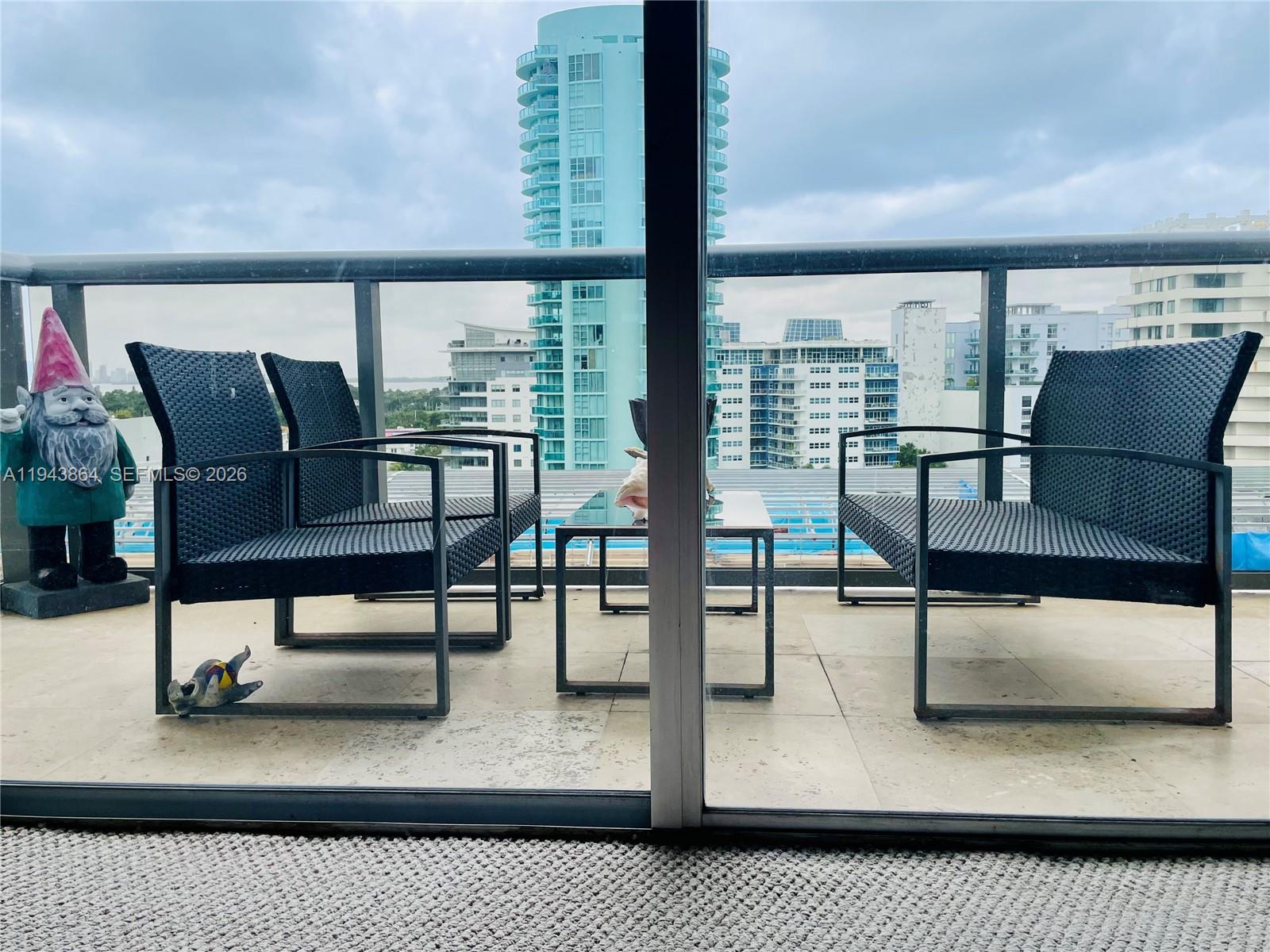 A balcony features three black wicker chairs, a small table, and a garden gnome — 6039 Collins Ave # 1232, Miami Beach FL 33140, MIAMI BEACH, FL