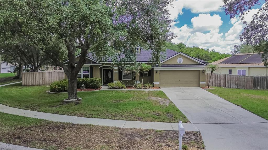 A single-story house with a tan exterior, a two-car garage, and a large front tree — 12426 WINDMILL COVE DRIVE, RIVERVIEW, FL